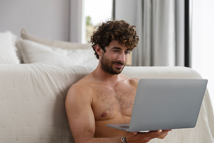 Homme lit torse nu avec ordinateur dans une chambre