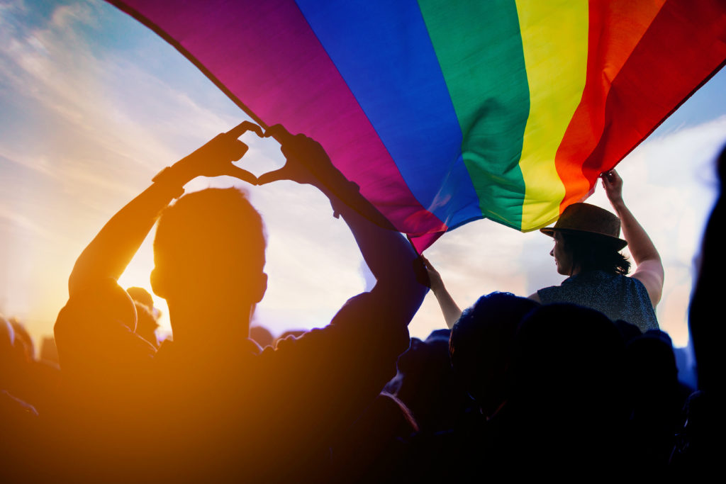 Homme qui fait un coeur avec un drapeau LGBTQ+